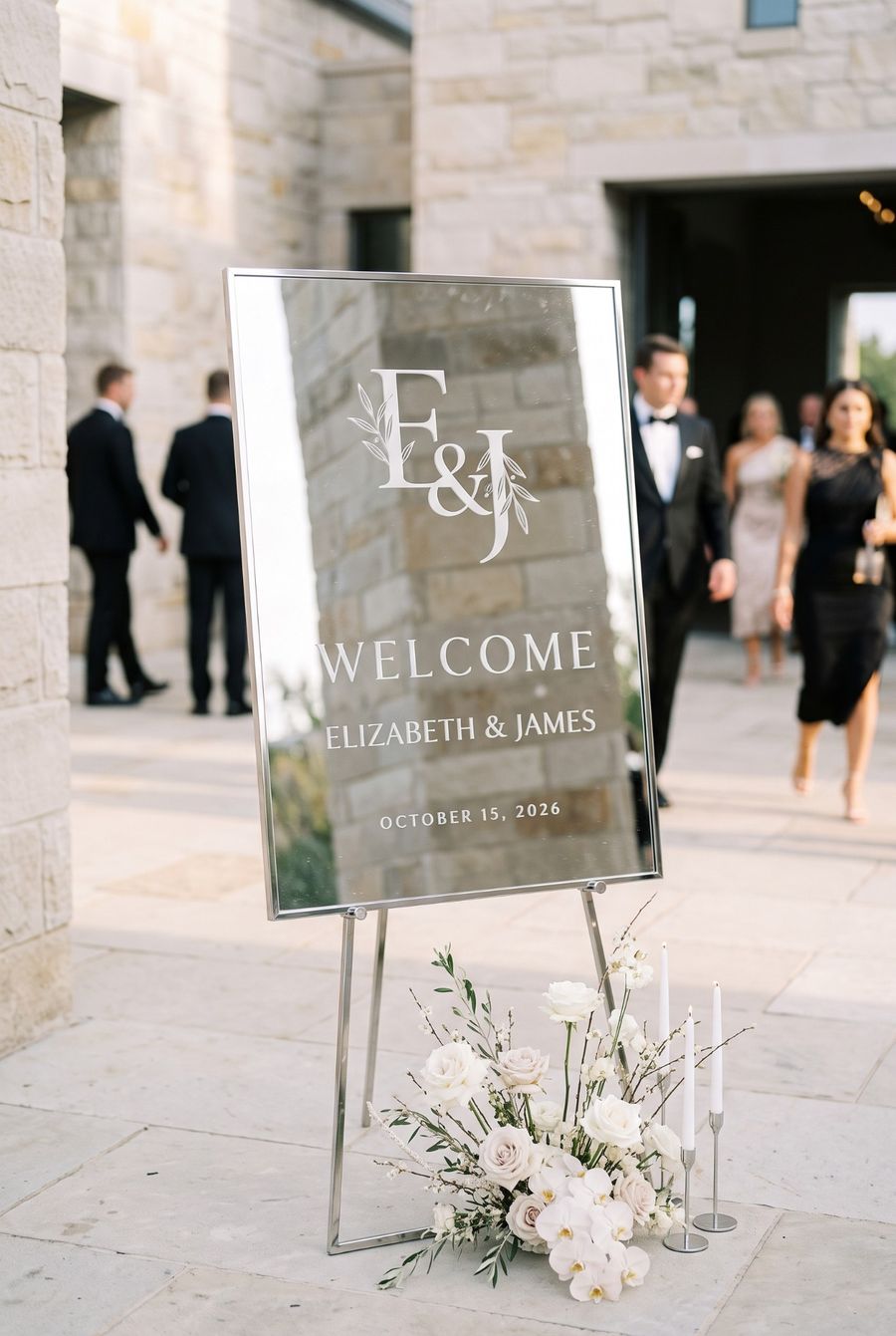 Silver-framed engraved mirror welcome sign with a modern monogram at a stone venue entrance